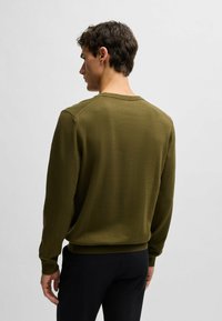 Maglione verde oliva lavorato a maglia con scollo rotondo, polsini e orlo a coste. Il tessuto ha una consistenza liscia e presenta un motivo uniforme.