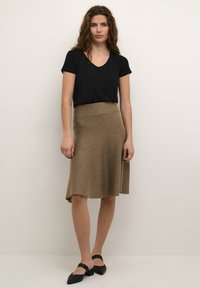 Zwarte V-hals t-shirt gecombineerd met een knie-lange, bruine, uitlopende rok. De rok heeft een zachte textuur en een gladde tailleband. Zwarte flats maken de look compleet.