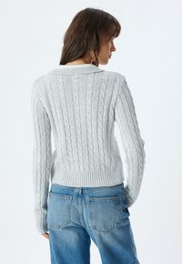 Maglione grigio chiaro a maglia cable con orlo e colletto a coste, caratterizzato da un motivo testurizzato. Abbinato a jeans in denim blu a vita alta.