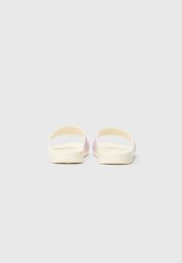 Sandálias rasas com base creme clara e riscas em rosa pastel, apresentando parte de trás e laterais abertas para ventilação. Textura lisa, semelhante a borracha.