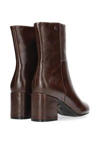 Botas de tobillo de cuero marrón con un tacón grueso, textura suave, detalles de costura lateral y acento de logo circular en el lado exterior.