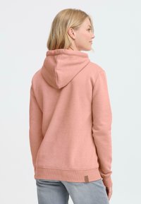 Un hoodie rose avec une texture douce, une capuche à cordon de serrage, des poignets et un bas côtelés, présentant une petite étiquette marron en bas à gauche.