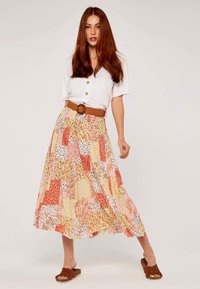 Blumen- und gemusterter Maxiskirt in Gelb, Orange und Weiß, mit einem gestuften Design und Taillengürtel; kombiniert mit einer weißen Button-Down-Bluse.