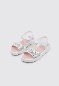 Sandalias blancas con un patrón de flores perforadas en la correa, plantilla rosa y una suela de goma texturizada blanca. Correa ajustable en el tobillo para un mejor ajuste.
