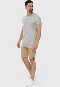 Grå t-shirt med sorte prikker, parret med beige shorts med en foldet kant og sidelukning. Hvide sneakers fuldender looket.