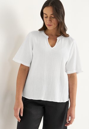 Witte, gestructureerde blouse met een V-hals en korte mouwen, met een ontspannen pasvorm en subtiele horizontale lijnen. Draagt met zwarte broek.