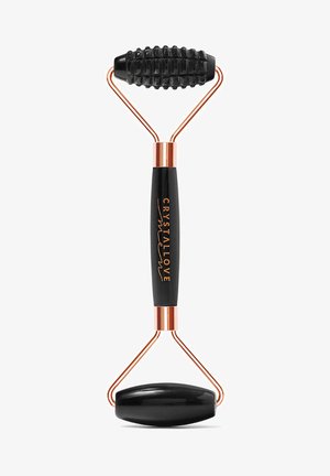 Rouleau facial noir avec une pierre ovale lisse à une extrémité et un rouleau texturé à stries de l'autre, reliés par des bras en métal de ton cuivre.