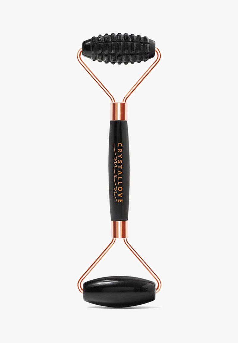 Czarny wałek do twarzy z gładkim owalnym kamieniem na jednym końcu i teksturowanym, rowkowanym wałkiem na drugim, połączony metalowymi ramionami w kolorze miedzi.