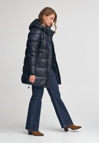 Svart puffjacka med huva, med quiltat mönster, framtida dragkedja och snörning. Kombinerad med mörka utsvängda jeans och bruna klackstövlar.