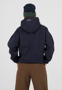 Granatowy hoodie z dużym kapturem i luźnym krojem, z haftowanym logo z tyłu, w połączeniu z brązowymi, strukturalnymi spodniami z szerokimi nogawkami.