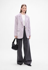 Svetlofialový kordový blazer s jedným gombíkom, v kombinácii s voľnými tmavosivými nohavicami. Čierna kabelka dotvára outfit.