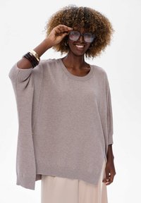 Jasnoszary, oversize sweter z prążkowanym okrągłym dekoltem i szerokimi rękawami, z bocznym rozcięciem i miękką teksturą. Uzupełniony bransoletkami.