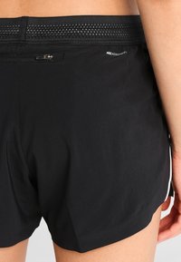 Pantalones cortos deportivos negros con una cinturilla texturizada, un pequeño bolsillo con cremallera y un logo de Nike. La tela parece ligera y suave.