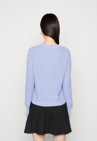 Suéter de punto azul claro con cuello redondo y dobladillo acanalado, que presenta mangas largas con acentos texturizados. Combinado con una falda negra.