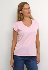 T-shirt en coton rose avec un col en V et des manches courtes. Texture douce, design décontracté, associé à un jean en denim bleu.