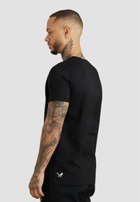 Schwarzes T-Shirt mit kurzen Ärmeln und rundem Halsausschnitt. Weicher Stoff, mit weißem, gekreuztem Schwert-Logo am unteren Saum.