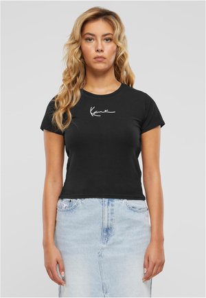 Zwarte katoenen t-shirt met korte mouwen, aansluitend ontwerp, en witte handtekeningafdruk op de borst, gecombineerd met een lichtblauwe spijkerrok.