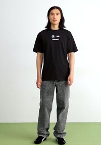 Sort bomulds t-shirt med "Motorsport" tekst og logo, parret med grå strukturerede denim jeans. Fodtøjet har et sort og hvidt design.