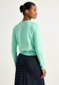 Mintgrön figurnära tröja med rund halsringning, långa ärmar och ribbade muddar, kombinerad med en marinblå kjol med prickar. Texturerat stickat tyg.