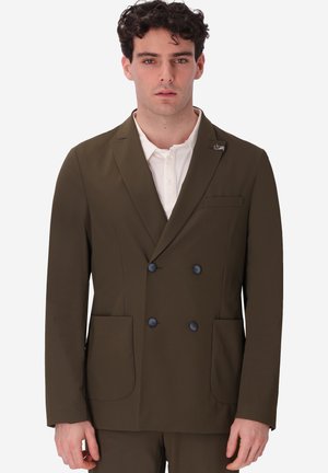 Uomo che indossa blazer doppiopetto color oliva con bottoni neri e due tasche applicate frontali sopra una camicia bianca con colletto.