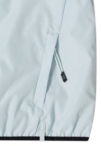 Lichtblauw jassenstuk met een schuin geplaatste ritszak met witte trekkoorden en zwarte bies, met het opschrift "CECIL OUTERWEAR".