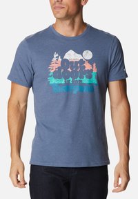 Camiseta corta de manga azul hecha de material suave, con un estampado gráfico de montañas y árboles en colores rosa y teal.