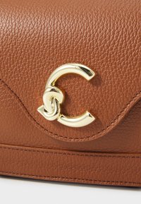 Brown textured leather bag with a gold C-shaped clasp and subtle stitching detail. Compact design with no visible hardware or patterns.