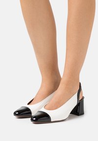 Slingbackové lodičky s bílým texturovaným svrškem a černou lakovanou špičkou. Nízký blokový podpatek, kulatá špička a otevřený zadní design.