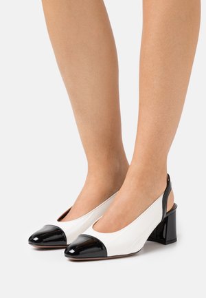 Sandały na obcasie typu slingback z białą teksturowaną cholewką i czubkiem z czarnej lakierowanej skóry. Niski obcas blokowy, okrągły nosek i otwarty tył.