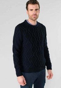 Dunkelblauer Strickpullover mit strukturiertem Wellenmuster, Rundhalsausschnitt und gerippten Bündchen. Der Stoff wirkt dick und warm, geeignet für kühlere Wetterbedingungen.