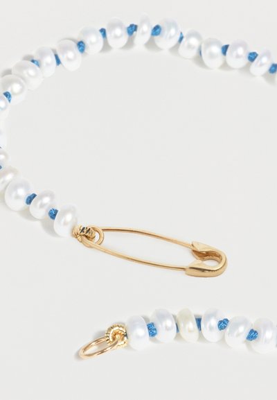 Κολιέ με λευκές πέρλες περασμένες σε μπλε νήμα, με χρυσό κούμπωμα ασφαλείας σε σχήμα παραμάνας και χρυσό δαχτυλίδι, σε λευκό φόντο.