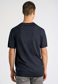 Marinblå kortärmad pullover med ett rent, strukturerat stickat mönster. Har en polo-krage och ribbade ärmslut och nederkant för en åtsittande silhuett.