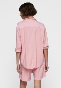 Lichtroze katoenen shirt met opgerolde mouwen en een ronde zoom, gecombineerd met bijpassende lichtroze shorts, gezien vanuit de achterkant.