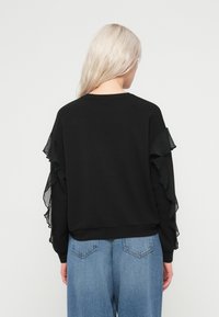 Czarny sweter z przezroczystymi, falbaniastymi rękawami. Miękki materiał o luźnym kroju, w połączeniu z jasnoniebieskimi, wysokimi dżinsami.