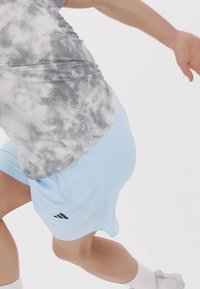 Svetlo modré športové šortky vo voľnom strihu s čiernymi logami, v kombinácii so šedým tričkom s batikovaným vzorom.