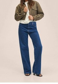Jeans z wysokim stanem i szerokimi nogawkami w kolorze niebieskim, wykonane z denimu, połączone z krótką oliwkową kurtką i białym swetrem z dzianiny. Widać płaskie sandały.