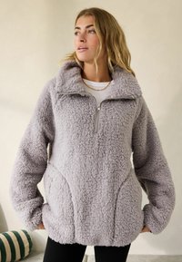 Uldent, lysegrå pullover med høj krave, halv lynlås foran, rummelige lommer og løstsiddende ærmer. Blød tekstur, afslappet design.