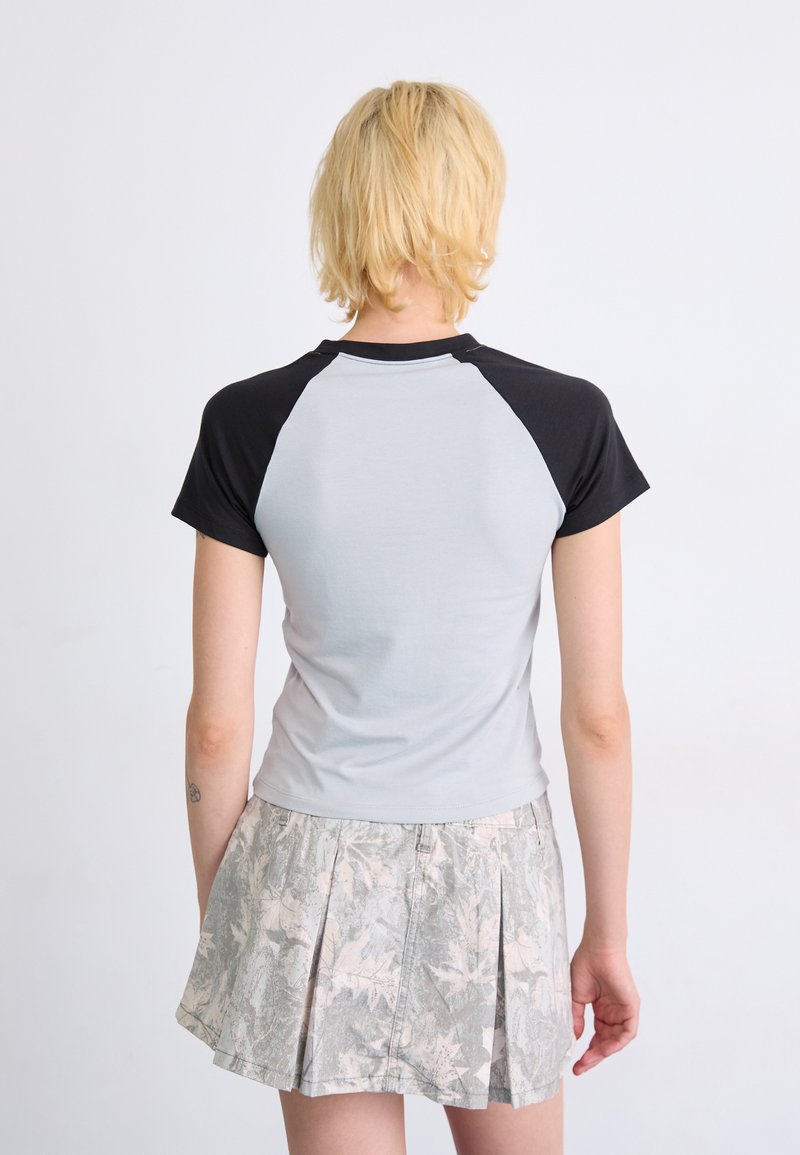 Camiseta de manga corta con diseño raglán negro, cuerpo gris y forma entallada, combinada con una falda plisada con un estampado de hojas.