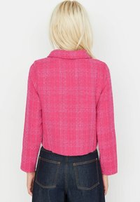 Roze cropped jack met een gestructureerd ruitpatroon, inkeping op de kraag en lange mouwen, gecombineerd met donkerdenim high-waisted broek.