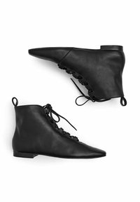 Juodi odiniai kulkšninių batai su smailiu nosiu, plokščiu kulnu, raištelių detalėmis šone ir lygiu paviršiumi.