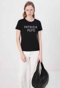 Melns īsās piedurknes T-krekls ar uzrakstu "PATRIZIA PEPE" sudraba rhinestones izpildījumā; valkāts ar baltām platām biksēm un melnu plecu somu.