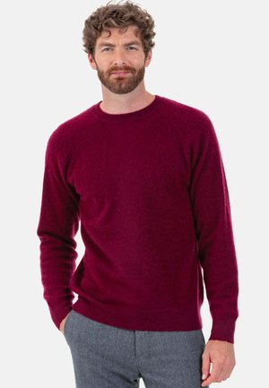 Strickpullover in tiefem Burgunderrot, Rundhalsausschnitt, lange Ärmel, leicht lockere Passform, strukturierter Stoff, kombiniert mit grauer Hose.