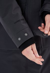 Svart vattentät jacka med en säker mudd med tryckknappar och ribbad stickad foder, med "W-Pro 10000"-logotypen präglad på ärmen.