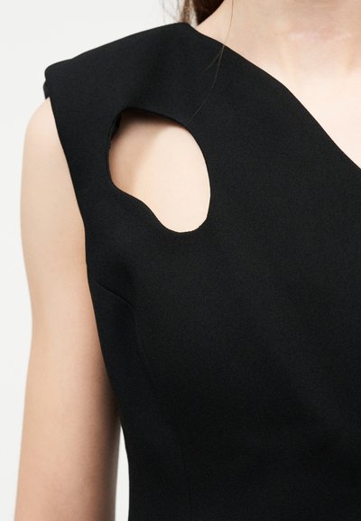 Haut noir sans manches avec découpe asymétrique près de l'épaule gauche laissant apparaître la peau.