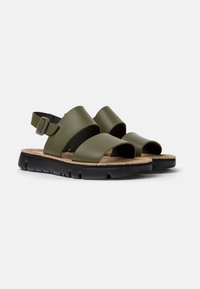 Olivgrønne sandaler med brede stropper, korkfodseng og sort gummisål. Justerbar ankelrem med metalspænde. Åben tå-design.