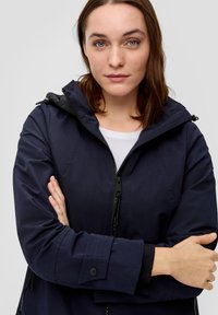 Marine waterdichte jas met een rits aan de voorkant, verstelbare capuchon en knoopmanchetten. Gladde textuur zonder zichtbare patronen of accenten.