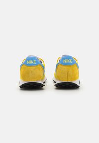 Mėlynos ir geltonos Nike sportbačiai su zomšos ir tinklelio tekstūromis, su paminkštintu apykaklės kraštu, raištelių sistema ir juodais gumos padais.