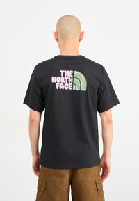 Sort bomulds t-shirt med et farverigt grafisk design på ryggen, der har teksten "THE NORTH FACE" og et grønt, buet designelement.
