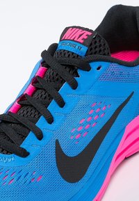 Modrá sportovní bota s růžovými akcenty, černými tkaničkami a výrazným logem Nike. Obsahuje síťované části a strukturovaný povrch pro prodyšnost.