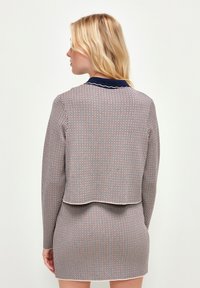 Stickad tröja med ett geometriskt mönster i marinblått, rött och vitt. Har en vågig krage och en kortad design med en texturerad yta.